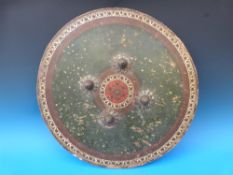 A tooled and painted circular shield with four metal studs