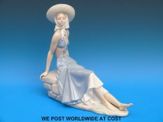 A Nao figurine of a girl in a sunhat reclining on a rock (29cm tall)