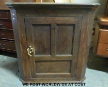An antique oak hanging corner cupbopard with panelled door,