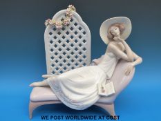 A large Lladro figurine of a lady reclining on a chaise longue with trellis backdrop (31cm tall)