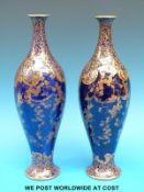 A pair of late 19th/20thC Royal Doulton pedestal vases with gilded decoration against a blue ground