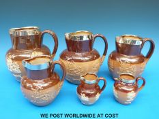 Six Doulton Lambeth graduated jugs all with hallmarked silver rims (largest 16.
