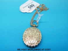 A Victorian mourning locket with chased foliate decoration on a yellow metal chain marked 9ct gold