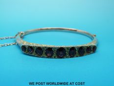 An Edwardian yellow metal bangle set with graduating oval garnets with alternating rose cut