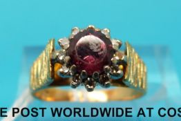 A yellow metal ring with bark effect shoulders set with a garnet and diamonds in a cluster (size J)