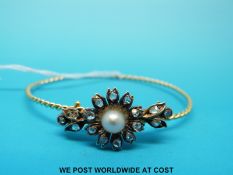 A yellow metal rope twist bangle set with a large pearl surrounded by 16 rose cut diamonds in a