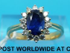 A yellow metal ring marked 18ct set with an oval sapphire surrounded by diamonds (size M)