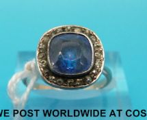 A yellow metal ring set with a cushion cut sapphire surrounded by diamonds (size N)