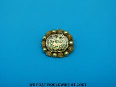 A yellow metal brooch with a deer to the centre surrounded by a border of spheres