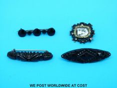 Four jet mourning brooches, one depicting an urn to the centre.