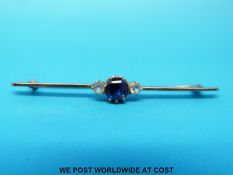 A yellow metal brooch set with a square cut sapphire flanked by white sapphire to each side