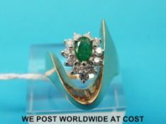 A yellow metal ring marked 14ct set with a pear cut emerald surrounded by diamonds in a wave design