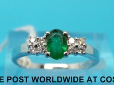 An 18ct white gold ring set with an oval cut emerald and four diamonds to each shoulder