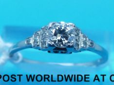A white metal Art Deco ring set with a round cut diamond with diamond encrusted shoulders (size O)