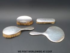A hallmarked silver hand mirror and three silver mounted brushes