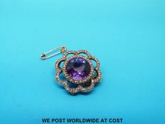 A yellow metal brooch set with an amethyst surrounded by diamonds