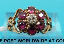 A 9ct gold ring set with a central diamond surrounded by rubies in a flower cluster with scrolling