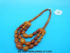 An amber necklace consisting of 55 graduated ovoid beads in three strands with crescent shaped