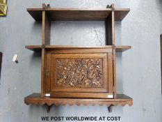 An Arts & Crafts style oak wall unit with small hinged cupboard carved with oak leaves and acorns,