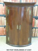 A Georgian bow fronted mahogany corner cupboard with brass hinges (H107 x W75 x D51cm)