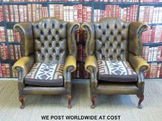 A pair of leather Chesterfield wing back armchairs with button backs and metal stud decoration,