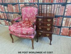 An upholstered armchair together with a reproduction serpentine fronted chest of four drawers