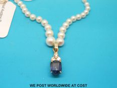 A single strand of pearls with a gold pendant set with a large sapphire and three diamonds