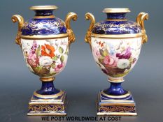 A pair of English porcelain pedestal urns with twin ram mask handles and hand decoration of flowers