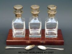 A set of three silver topped bathroom glass bottles on mahogany stand, width 25.