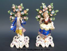 A pair of male and female porcelain figures standing before flowering trees,