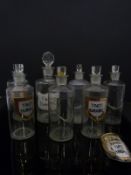 Six glass apothecary bottles with gilt labels (all 18cm tall) together with one similar (21cm tall)