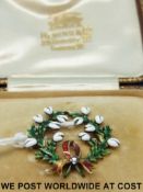 A yellow metal brooch set with enamel in the form of a wreath with a diamond set bow to the bottom,