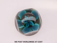 A faceted glass paperweight with central blue flower over mottled ground with red and white cane to