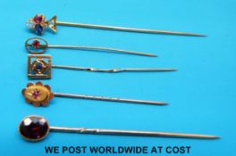 Three yellow metal stick pins, one set with a sapphire, one ruby and the other garnet,