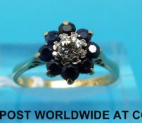 A yellow metal ring marked 18ct set with a round brilliant cut diamond surrounded by sapphires in a