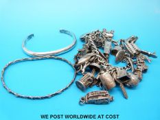 A silver charm bracelet with a large quantity of silver charms and two silver bangles