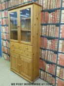 A pine display cabinet with glazed doors above two drawers over cupboards (W105 x H203 x D35cm)