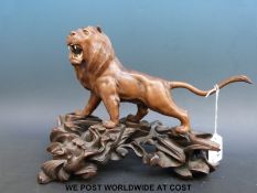 A Chinese carved wooden model of a lion with amber eyes and bone teeth on carved hardwood stand