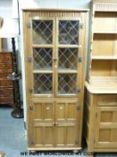 A light oak glazed corner cupboard in the Arts and Crafts style (H169 x W68 x D35cm)