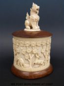 A carved ivory pot with relief decoration of elephants and figures with a wooden base and top with