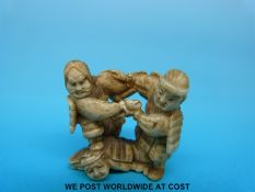 A Japanese Meiji period carved ivory netsuke of two Samurai fighting on the back of another Samurai
