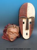An African tribal mask with painted decoration and a mask with bird to the top and fabric 'hair'