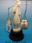 An early 20thC carved Indian ivory figure of an artisian in native clothes carrying pots,