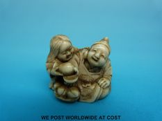 A Japanese Meiji period signed carved ivory netsuke of two laughing figures pouring sake from a
