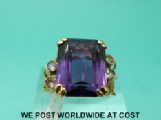 A yellow metal ring marked 14k set with a large purple sapphire with clear stones to the shoulders