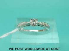 A 9ct white gold ring set with a round brilliant cut diamond with diamond encrusted shoulders,
