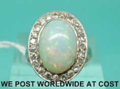 An Art Deco 18ct white gold ring set with an oval opal cabochon surrounded by diamonds (size L)