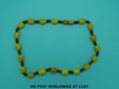 An amber necklace of 21 egg yolk coloured oval beads interspersed with white metal open wirework