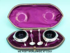 A cased pair of hallmarked silver open salts with blue glass liners