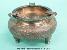 An Eastern white metal three footed ashtray decorated with land and seascapes,